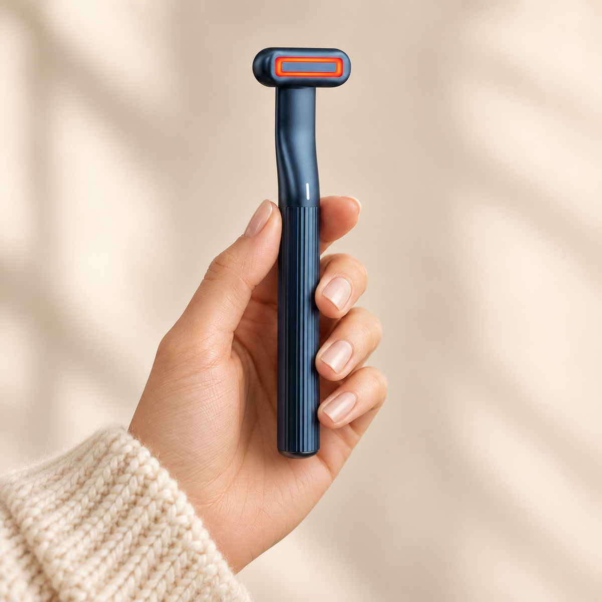 Hand holding the Auva Glow Wand showing slim ribbed navy body and glowing red light head